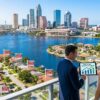 Tampa real estate agent showing couple rising inventory data on tablet overlooking Tampa Bay waterfront with multiple for sale signs on homes and downtown skyline