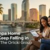 Professional couple reviewing Tampa home prices falling chart on tablet with downtown Tampa skyline, waterfront, palm trees and for sale sign at golden hour